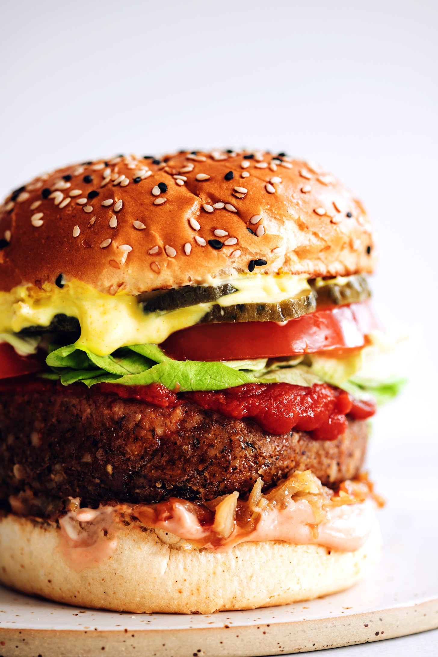 Közelkép lövés egy zsemle savanyúsággal, mustárral, paradicsommal, salátával, ketchuppal, vegán burger pogácsával, karamellizált hagymával és sriracha majonézzel