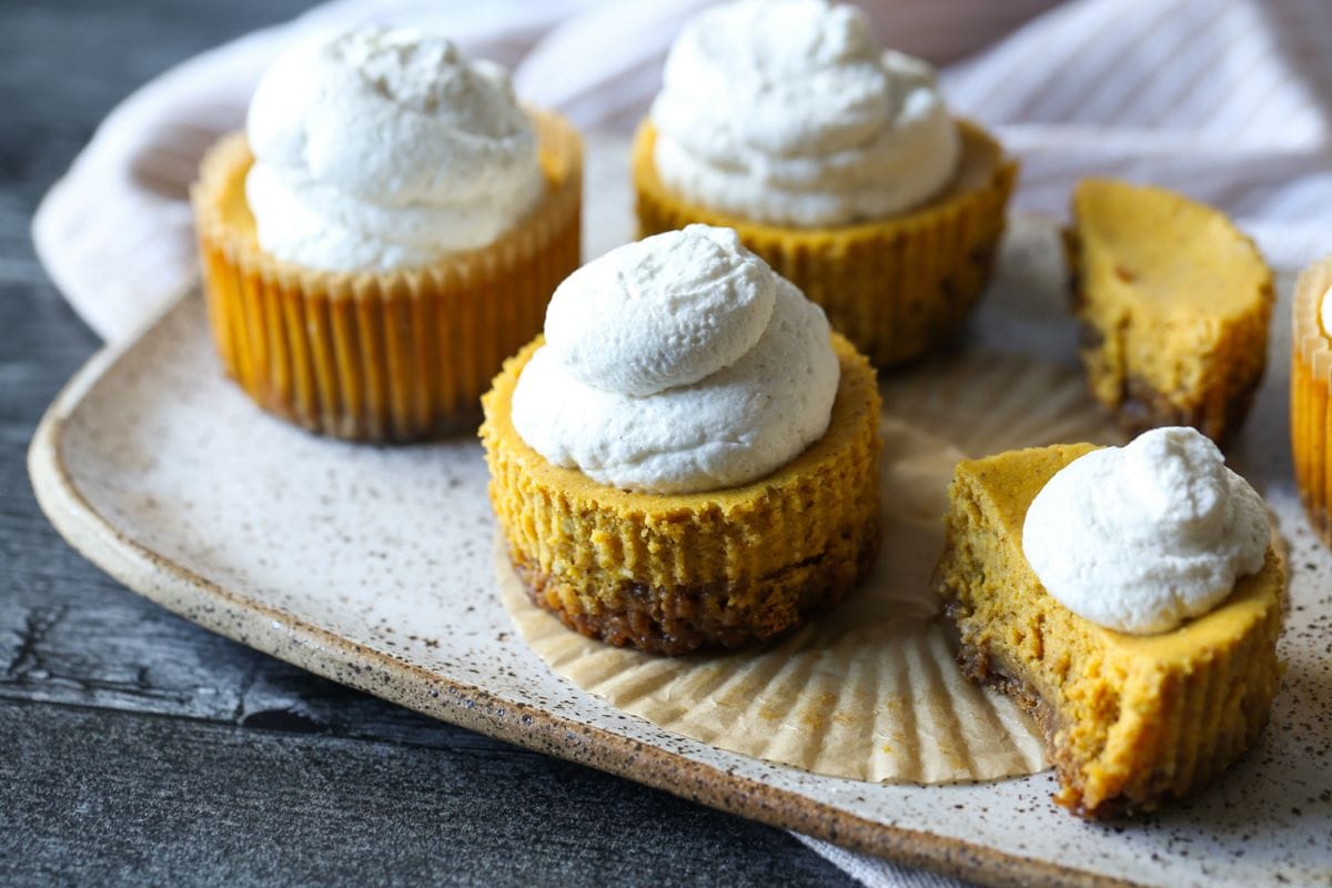 Mini pumpkin cheesecakes on a baking sheet, one cut open to reveal the middle.