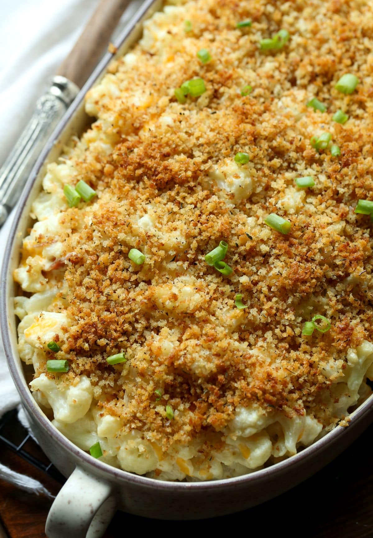 A baked cauliflower casserole topped with breadcrumbs and garnished with green onions.
