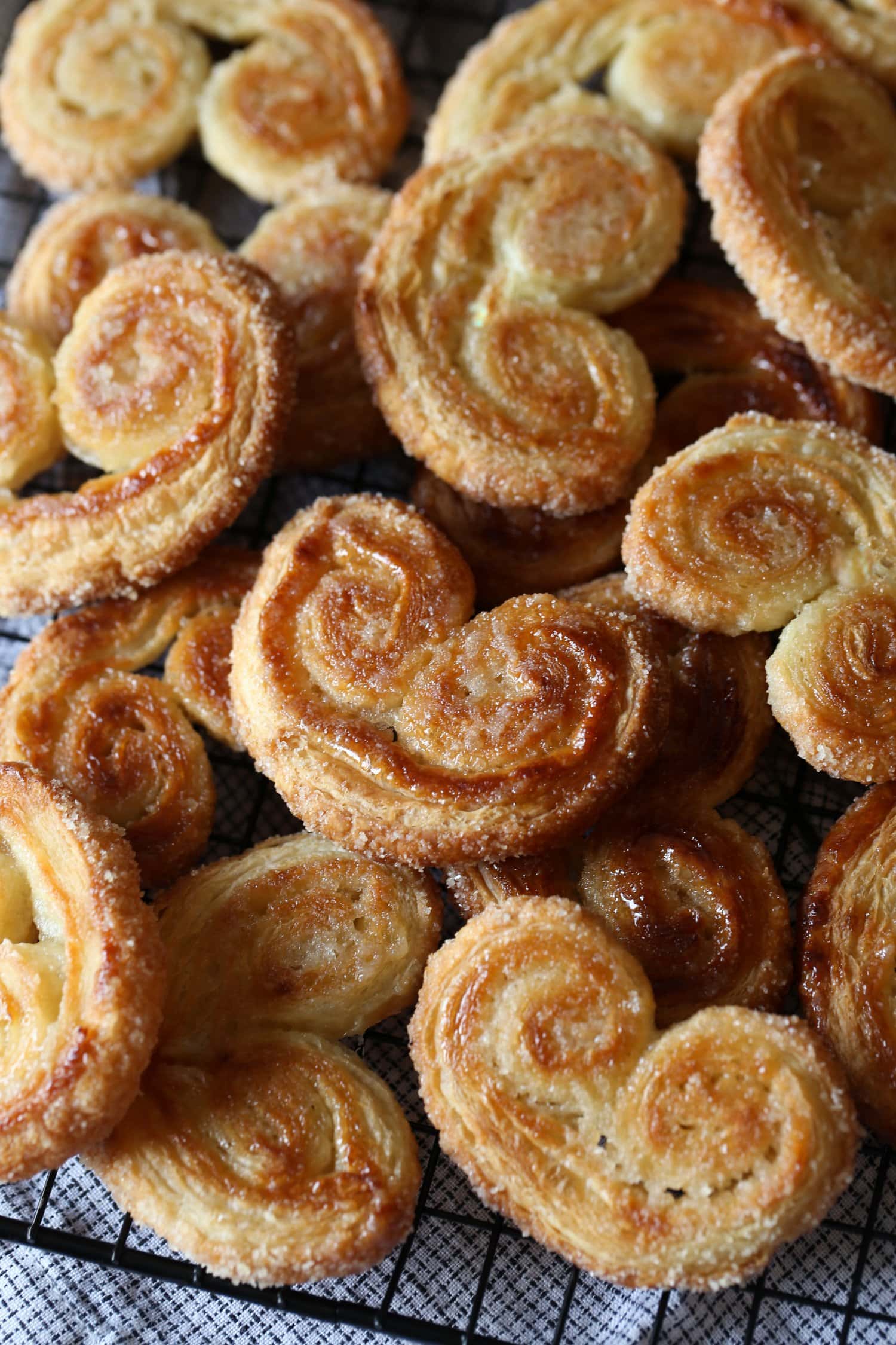 An assortment of crunchy and golden palmier cookies piled over a wire rack.